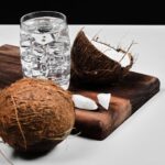 cocco-tagliato-a-meta-su-tavola-di-legno-e-bicchiere-d-acqua-con-ghiaccio_114579-62055